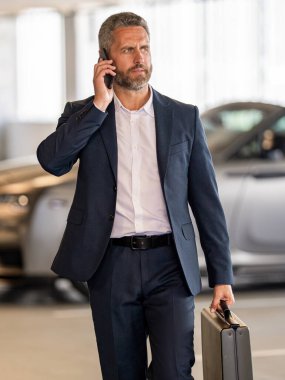 Busy businessman talking on phone outdoor. Businessman using phone at parking. Man phone conversation. Hispanic business man with smartphone. Business communication. Man reply phone call.
