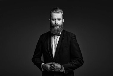 Sakallı damat kendinden emin ve hırslı hissediyor. Smokinli erkek giysili adam Griler 'de izole edilmiş. Smokinli adam resmi erkek giyim bölümünde. Yakışıklı sakallı adam smokin giyer. Şık smokin papyonu. Gerçek zarafet.