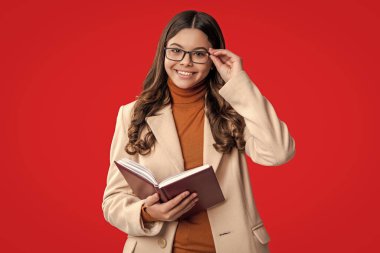 Kız kitap okuyor. Okuma öğrencisi. Gözlüklü liseli kız kitap okuyor. Bilgi ve eğitim. Okula dönelim. Sonbahar montlu ergen kız kırmızıda izole edilmiş. Kitap okuyucu. 1 Eylül.