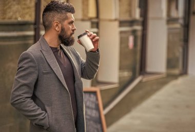 Günlük iş rutini. Sakallı adam şehir caddesinde kahve içiyor. Sokakta elinde kahve tutan yakışıklı bir adam. İş hayatı, mola. Sabah kahvesi içen adam. Kahve molası, afiş.