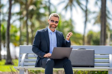Successful businessman freelancing online. Business success. Businessman working on laptop outdoor. Business man typing on laptop on the bench. Business man working online.
