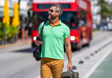 Yaz gezisi için seyahat valizi. Yaz gezisini ayarlayan adam. İspanyol turist gezginleri kitabı internette. Seyahat çantalı bir turist. Gezgin telefon kullanıyor. Turist tatili rezervasyonu. Online biletler.