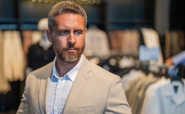 Bespoke terziliği. Takım elbiseli bir erkek model. Perakende satış asistanı şık bir adamın takım elbise bulmasına yardımcı olur. Takım elbiseli şık bir adam. İşadamı şık bir takım seçmiş. Moda ceket. Boşluğu kopyala.