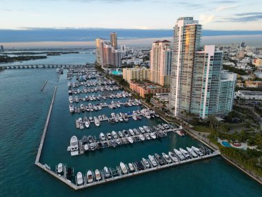 Miami marinasındaki lüks yatların hava manzarası. Miami marinasındaki tekne ve gökdelenlerin manzarası. Miami kıyı şeridi boyunca seyir yatı. Miami Sahil Limanı. İskelede yelkenliler ve yatlar