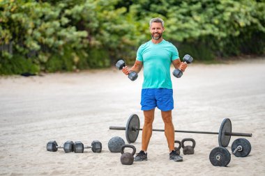 Sağlıklı yaşam stili eğitimi. Güçlü adam dambılla dışarıda egzersiz yapıyor, afiş. Erkek atlet dambılı kaldırıyor. Güçlü adam spor egzersizi yapar. Jimnastik. Dambılı bir sporcu..