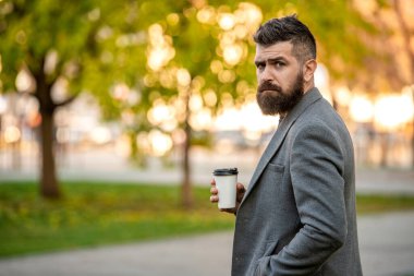 Sabah kahvesi içen adam. Kahve molası. Günlük stil rutini. Sakallı adam sonbahar şehrinde kahve içiyor. Sonbahar adamı elinde kahve fincanıyla parkta. İş hayatı, mola zamanı. Boşluğu kopyala.