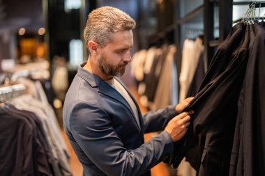 Bespoke terziliği. Butikte iyi giyimli erkek model. Perakende satış asistanı şık bir adamın takım elbise bulmasına yardımcı olur. Takım elbiseli şık bir adam. İşadamı şık bir takım seçmiş. Moda kıyafeti.