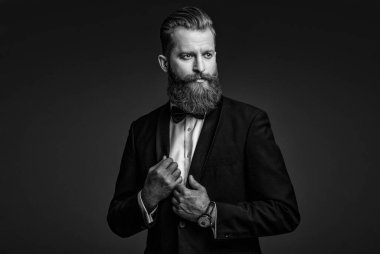 Yakışıklı sakallı adam smokin giyer. Şık smokin papyonu. Sakallı damat kendinden emin ve hırslı hissediyor. Smokinli erkek giysili adam Griler 'de izole edilmiş. Smokinli adam resmi erkek giyim bölümünde. Mükemmel biçim.