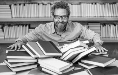 Okul kütüphanesinde dahi öğretmen. Kitap yığınında ev ödevi edebiyatı okumak dahice. Erkek öğretmen kitap okudu. Üniversitede okul eğitimi. Bilgi günü. Kitap kurdunun fazla çalışması. eğitim edebiyatı.