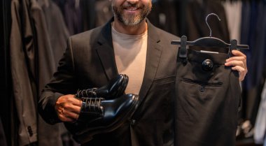 Terzi elbisesi seçen bir iş adamı manzarayı kesmiş. Bespoke terziliği. Takım elbise butiği içinde iyi giyimli erkek manken. Perakende satış asistanı şık bir adamın takım elbise bulmasına yardımcı olur. İşadamı şık bir takım elbise seçmiş..