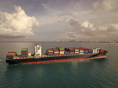 Hava görüntülü kargo gemisi limana giriyor. Kargo işi. Konteyner gemisi. Nakliye lojistiği. Kargo gemisi denizde, hava manzaralı. Yük konteynırı kargo gemisine yüklendi. Yük konteynırları üst üste dizildi.