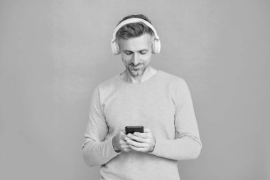 Kulaklıklı adam telefonda mp3 çalma listesini seçiyor. Akıllı telefon uygulaması kullanan adam mavi ile izole edilmiş. Telefonla müzik dinlemek. Müzik yaşam tarzı. Ses çalma listesi. Kulaklıklı adam..