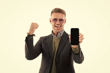 Mutlu iş adamı telefon ekranını sunar. İş adamı, telefonun beyazda izole olduğunu gösteriyor. Adam yeni iş telefonu uygulamasını gösteriyor. Başarıyı ifade etmek. Ürünü sunuyorum. İş uygulamasının reklamı.