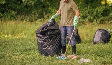 Çevre gönüllüsü. Ormanda çöp toplama. Ekoloji konsepti. Çöp toplama gönüllüsü, ekoloji. Çöp torbasıyla lastik eldivenli adam çöpü temizliyor. Adam plastik çöp topluyor. Ev atıkları.