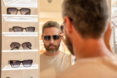 Dükkanda güneş gözlüğü seçen bir adam. Moda mağazasında güneş gözlüğü mankeni. Modaya uygun bir adam. Erkekler için moda güneş gözlüğü aksesuarları. Göz giysisi koleksiyonu. Güneş gözlüklü, seçici odaklı moda görünümü.