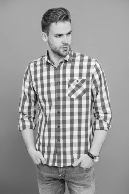 Sıradan tişörtlü bir adamın portresi. Tıraşsız adamın zarif portresi. Gri yolda izole edilmiş bir adam. Kareli gömlek giyen milenyum adamı. Milenyum erkeğinin gündelik tarzı. Sıradan şıklık..