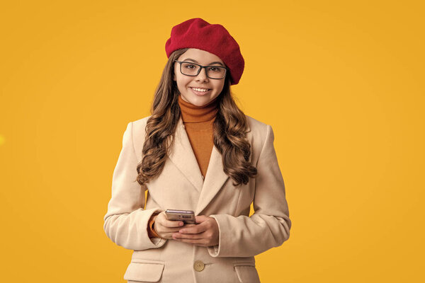 Adolescence generation. Adolescent girl with phone. Autumn girl using phone isolated on yellow. Teen happy girl in autumn style beret and coat. Fall style. Girl chatting on phone. Timelessly stylish.