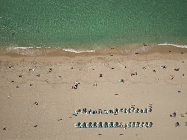 Yazın deniz kenarında tatil. Deniz, plaj şemsiyesi altında rahatlar. Denize açılın. Kristal berrak turkuaz suyla kumsalın havadan görünüşü. Cennette yaz tatili.