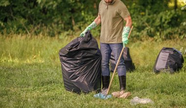 Çevre gönüllüsü. Ormanda çöp toplama. Ekoloji konsepti. Çöp toplama gönüllüsü, ekoloji. Çöp torbasıyla lastik eldivenli adam çöpü temizliyor. Adam plastik çöp topluyor. Ev atıkları.