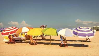 Denize açılın. Şemsiyeli kumlu egzotik plaj. Plaj güneşinde güneşli bir hava. Yaz tatili. Yazın deniz kenarında tatil. Seyahat acentesi. Deniz, plaj şemsiyesi altında rahatlar. Yaz zamanı..