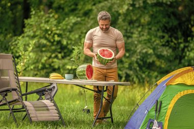 İspanyol adam kamp yapıyor. Karpuz kampı pikniği. Lezzetli sağlıklı yiyecekler. Kampta taze yiyecek. Yaz kampında karpuzlu bir adam. Yaz günü doğa yürüyüşçüsü. Kamp ve doğa pikniği.