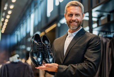 Ayakkabı mağazasındaki tezgahtar adam klasik ayakkabıları tutuyor. Ayakkabı mağazası. İş adamı dükkanda şık ayakkabılar seçer. Resmi görünmek için klasik deri ayakkabılar. Resmi ayakkabı. Deri ayakkabı reklamı.