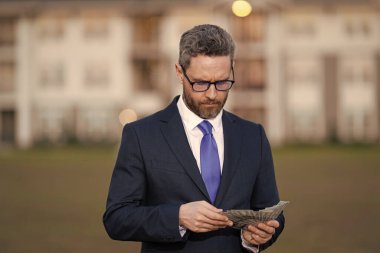 Evin sahibi dışarıda para tutuyor. Emlakçı yeni bir ev teklif ediyor. Komisyoncu teklifte bulundu. İşadamı komisyoncu para sayar. Emlak konsepti. Para dolu takım elbiseli başarılı bir emlakçı. Özellik listeleme uzmanı.