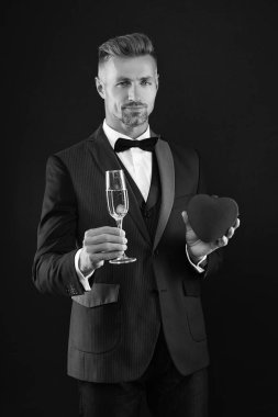 Smokinli ve şampanyalı zengin bir adam. Sevgililer günü indirimi. Zengin adam sevgililer gününü kutluyor. Yürekli bir adam. Sevgililer günün kutlu olsun. Sevgi dolu bir adam siyahta izole edilmiş. Romantik hediyelere bayılırım. Aşk teklifi.