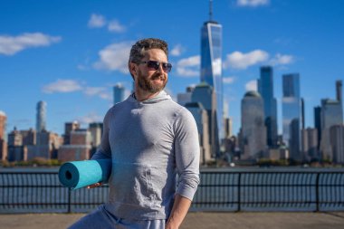New York 'ta sporcu. Manhattan 'da spor kıyafetli bir adam. Vücuduna uygun. Yoga koçu. Sporcu adam antrenmana hazır. Sağlıklı bir yaşam tarzı. Spor ve spor. Eğitim için yoga minderi, kopyalama alanı.