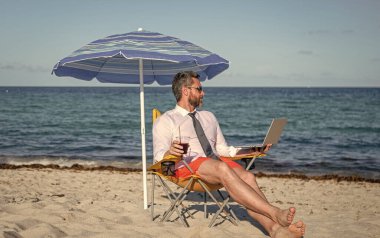 Seyahat ve iş. Sea Beach 'te serbest çalışan bir adam. Yazın iş adamı. Çevrimiçi serbest çalışma. Dizüstü bilgisayarı olan bir işadamı. Kumsalda dizüstü bilgisayar kullanan bir iş adamı.