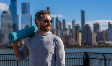Eğitim için yoga minderi. New York 'ta sporcu. Manhattan 'da spor kıyafetli bir adam. Vücuduna uygun. Yoga koçu. Sporcu adam antrenmana hazır. Sağlıklı bir yaşam tarzı. Spor ve spor. Spor paspası.