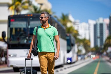 Yaz turu. Gezgin yaz tatilinin tadını çıkar. Sokakta yürüyen İspanyol turist. Tropikal şehirde bavullu bir turist. 40 'lı yılların turisti yaz tatilinde. Seyahat valizi, pankart..