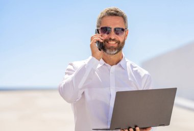 İş başarısı. Adam maili kontrol ediyor. Başarılı iş adamı çevrimiçi olarak serbest çalışıyor. Açık havada serbest çalışan bir iş adamı. Serbest geliştirici internet üzerinden iş yapıyor. İş adamı telefonda konuşuyor..