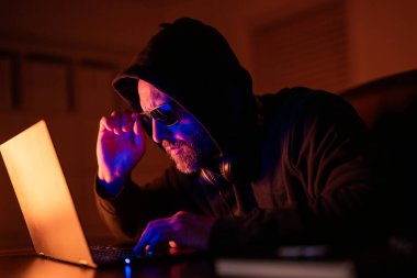 Siber saldırı. Siber suçlular ve çalınan finansal veriler. Dijital para hırsızı. Ofis laptopunda kapüşonlu bilgisayar programcısı, oyun. Hacker saldırısı. Geceleri ofiste bilgisayar korsanı. Gece yarısı hackerı.