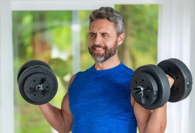 Güçlü trisepsler. Dambılla egzersiz yapan bir adam. Erkek atlet dambılı kaldırıyor. Güçlü adam spor egzersizi yapar. Jimnastik. Dambılı bir sporcu. Ağır dambıllar, kas kasları..