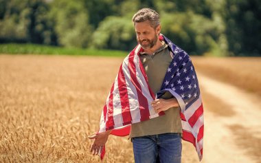 Ekin tarlasında Amerikan bayrağı taşıyan adam. Amerika 'nın Bağımsızlık Günü. 4 Temmuz. Amerikan İşçi Bayramı. Amerikan bayrağı ve çiftçi adam. ABD bayrağı. Bağımsızlık Günü. Sahadaki adam, reklam..
