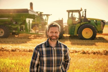 Kareli tişörtlü çiftçi ziraatçi adam hasat makinesiyle hasat hasadıyla tarlada duruyor..