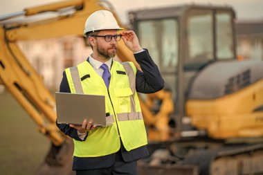 Hardhat 'ın baş mühendisi dizüstü bilgisayar kullanıyor. İş projesi. İnşaat mühendisi. Denetçi işçi. Şantiyedeki adam. İnşaat projesi. Uzayı kopyala Bina planlama çalışması.