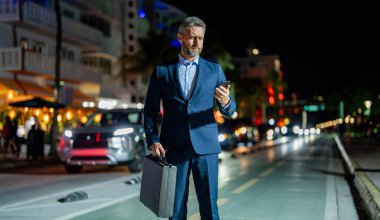 Gece vakti yürüyen iş adamı. Dışarıdaki telefonda iş adamı sohbeti. Gece caddesinde iş adamı telefonda konuşuyor. Akıllı telefon kullanan bir iş adamı. Başarılı bir iş adamı internette sohbet ediyor. Şehir gecesi.