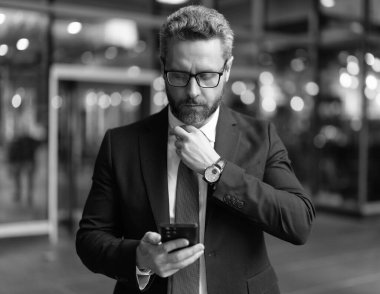 Modern mobil iş iletişimi. İş adamı telefonda mesaj atıyor. İş adamı kılığındaki bir adamın telefon mesajı. Telefon kullanımı. Dışarıdaki telefonda mesajlaşan bir adam. Meşgul adam iş mesajı okuyor.