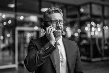 İletişim. İş adamı açık havada akıllı telefondan konuşur. Olgun iş adamı telefon görüşmesi yapar. İş görüşmesi. Takım elbiseli adam telefonda konuşuyor. Telefon var. Mobil iletişim.