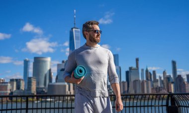 Manhattan 'da spor kıyafetli bir adam. Vücuduna uygun. Yoga koçu. Sporcu adam antrenmana hazır. Paspası esnetiyorum. Spor ve spor. Eğitim için yoga minderi. New York 'ta sporcu.