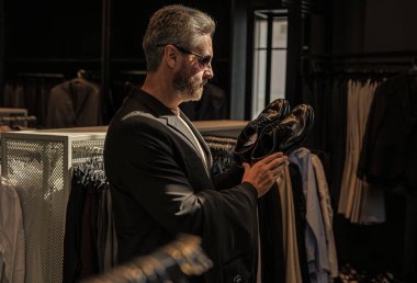 Ayakkabı mağazasındaki tezgahtar adam klasik ayakkabıları tutuyor. Ayakkabı mağazası. İş adamı ayakkabıyı dükkanda seçer. Resmi görünmek için klasik deri ayakkabılar. Resmi ayakkabı. Deri ayakkabılar. Ayakkabı görüntüsü düzenleniyor.