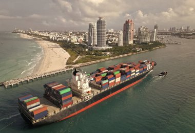 Miami Limanı. Miami 'de konteynırlı kargo gemisi, hava manzaralı. Kargo gemisinde nakliye konteynırı. Kargo gemisi limandan ayrılıyor. Konteyner gemisi. İhraç ve ithalat. Kargo işi. Miami plajı.
