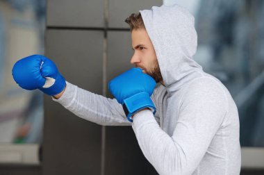 Boks antrenmanı. Boks eldivenli bir sporcu. Genç boksör. Sporcu boks. Güçlü bir atlet. Kapüşonlu sporcu. Spor giyim sektöründe güçlü bir boksör. Egzersiz ve yumruk. Ağır kanca.