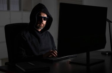 Ofis laptopunda kapüşonlu bilgisayar programcısı, oyun. Hacker saldırısı. Geceleri ofiste bilgisayar korsanı. Siber saldırı. Siber suçlu ve çalıntı kişisel veriler. Dijital hırsız. Güvenlik açığı.