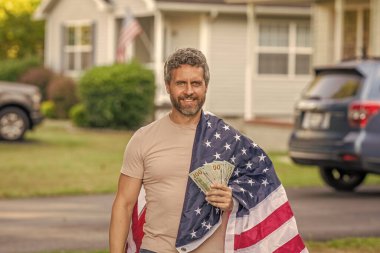 Vatansever adam. Amerikan bayrağı ve dolar parası olan adam. Enflasyon konsepti. Amerikan vergi politikası. İspanyol adam ve Amerikan bayrağı. Amerika 'da vergi ödemek. Katma değer vergisi. Vergi ve gümrük vergisi sistemi.