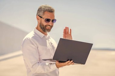 Video konferansı. Dışarıda dizüstü bilgisayarda çalışan bir iş adamı. Adamın iş görüşmeleri var. Başarılı iş adamı çevrimiçi olarak serbest çalışıyor. İnternette çalışan bir iş adamı. Uzaktan kumanda çalışıyor. Çevrimiçi iletişim.