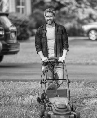 Kareli tişörtlü İspanyol adam banliyö arka bahçesinde çimenleri elektrikli çim biçme makinesi ve çim biçme makinesiyle kesiyor..