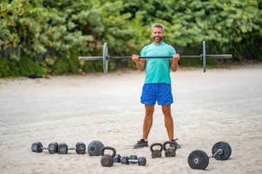 Sağlıklı yaşam halter eğitimi. Olgun bir adam halterle dışarıda egzersiz yapıyor. Erkek sporcu halter kaldırıyor. Güçlü adam spor egzersizi yapar. Jimnastik. Halterli sporcu, kopyalama alanı.